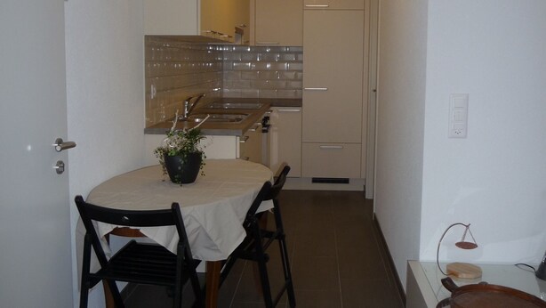 A compact kitchen with a dining area, featuring a round table, chairs, and a potted plant. - Nice countryside studio near city (Formangueires)