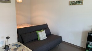 A modern living room with a grey sofa, a small table with photos, a hanging light, and a green plant on the wall. - Nice countryside studio near city (Formangueires)