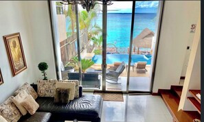 Una sala de estar con un sofá de cuero negro, una mesita y vistas a una piscina y al océano a través de grandes puertas correderas de vidrio.