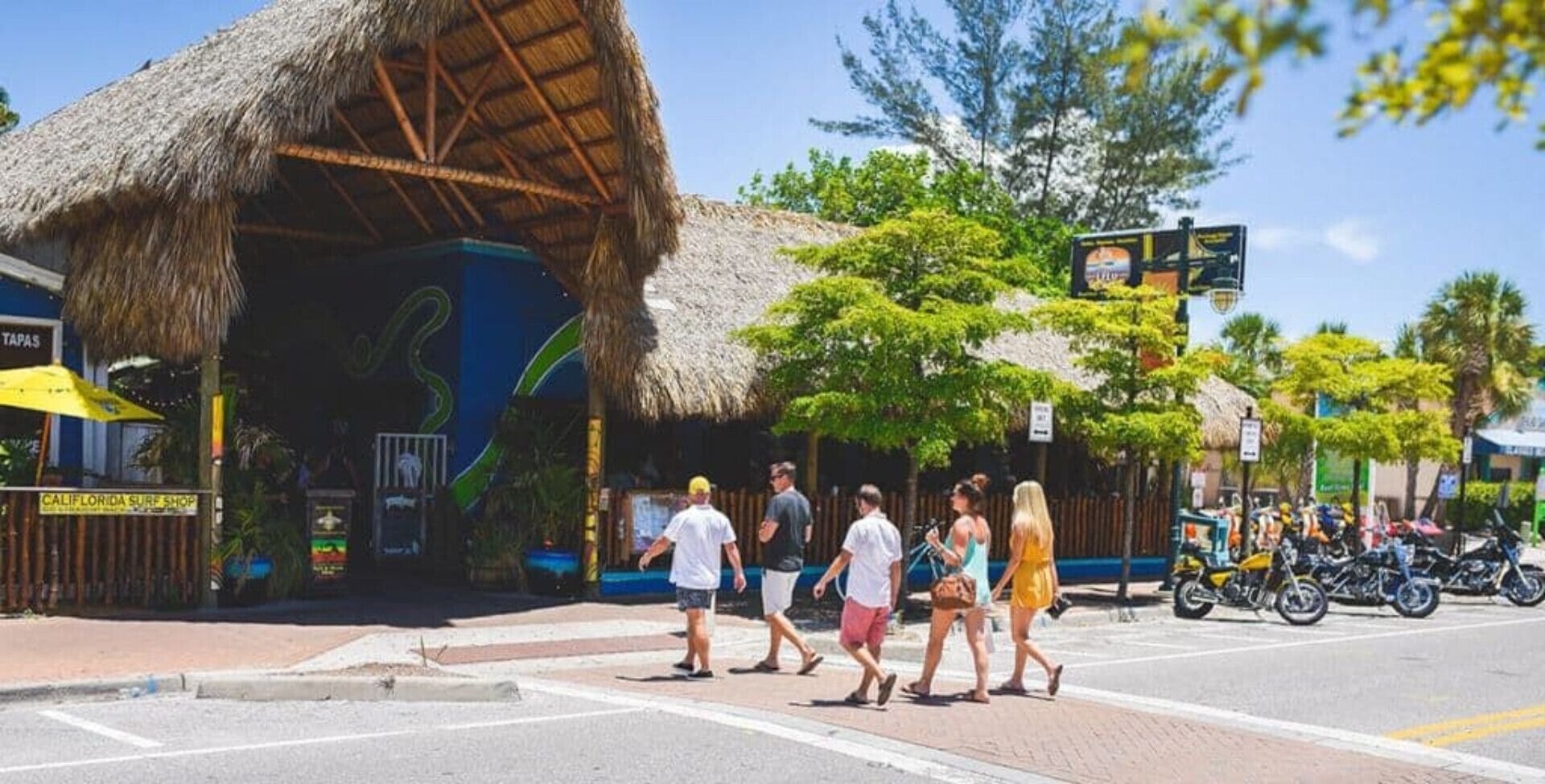 A street scene with a thatched-roof building, a surf shop, and a sign for a surf shop.
