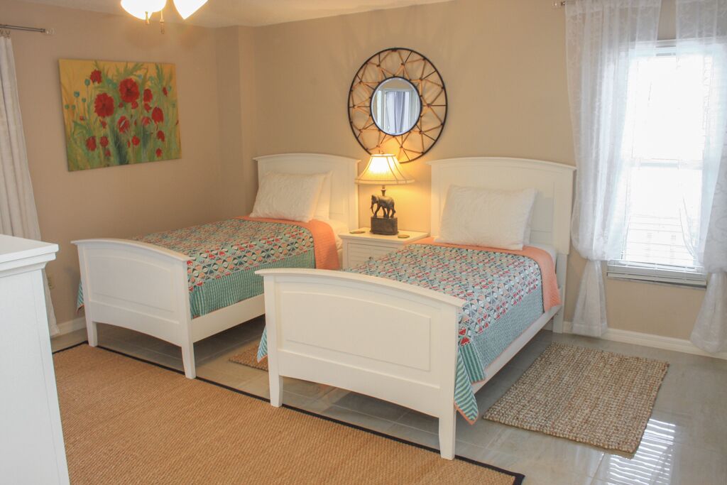 A bedroom with two single beds, a bedside table with a lamp, a wall mirror, and a painting.