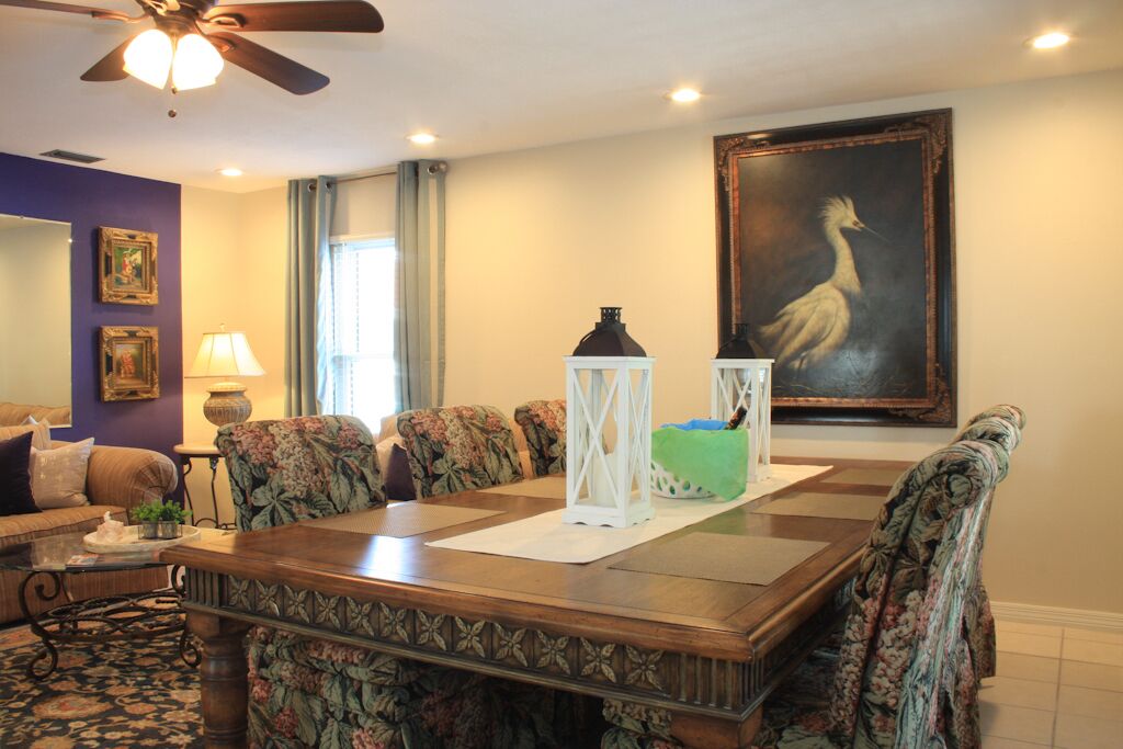 A dining area with a wooden table, floral-patterned chairs, a ceiling fan, and a painting on the wall.