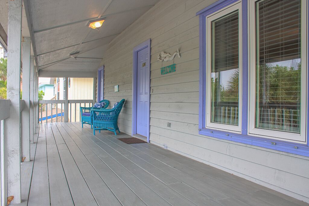 A covered porch with a wooden floor, a blue door labeled "Valerie," and a blue chair.