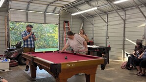 A pool table in a spacious room with a high ceiling and metal beams.