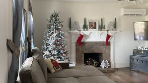 A living room with a sectional sofa, a fireplace, a Christmas tree, and a mounted TV.