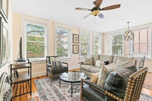 A living room with a sofa, armchair, coffee table, and a ceiling fan. - Old Met 202 | Downtown Mall | The 100 Collection (Charlottesville)