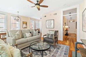 A living room with a sofa, armchair, coffee table, and a ceiling fan. - Old Met 202 | Downtown Mall | The 100 Collection (Charlottesville)