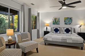 Relax in this inviting bedroom with a large bed, seating area, and large windows offering a view of the surrounding greenery.