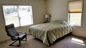 A bedroom with a bed, a chair, a nightstand, and two windows.