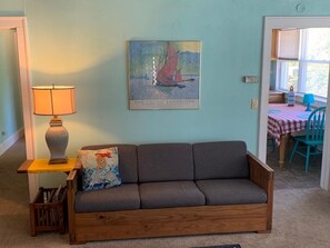 A room with a wooden sofa, a lamp, and a painting of a sailboat on the wall.