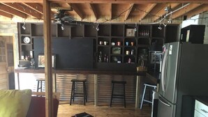 A cozy kitchen with wooden beams, a bar area, and a seating area with a red sofa and patterned cushions. - The Barn - Only 5 minutes to I65 (Montevallo)