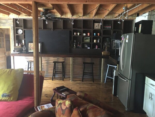 A cozy kitchen with wooden beams, a bar area, and a seating area with a red sofa and patterned cushions.
