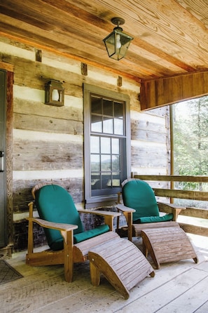 A rustic cabin with wooden walls, a large window, and two wooden lounge chairs with green cushions.