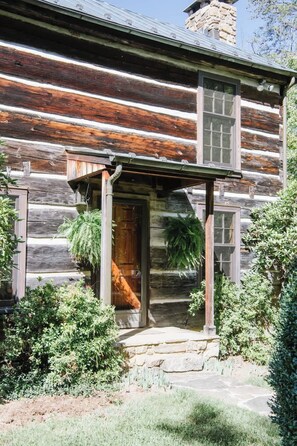 A rustic log cabin with a wooden porch, a stone foundation, and a chimney. - Tim`s Cabin | 1 BR Cabin w/ View of Mountains (Earlysville)