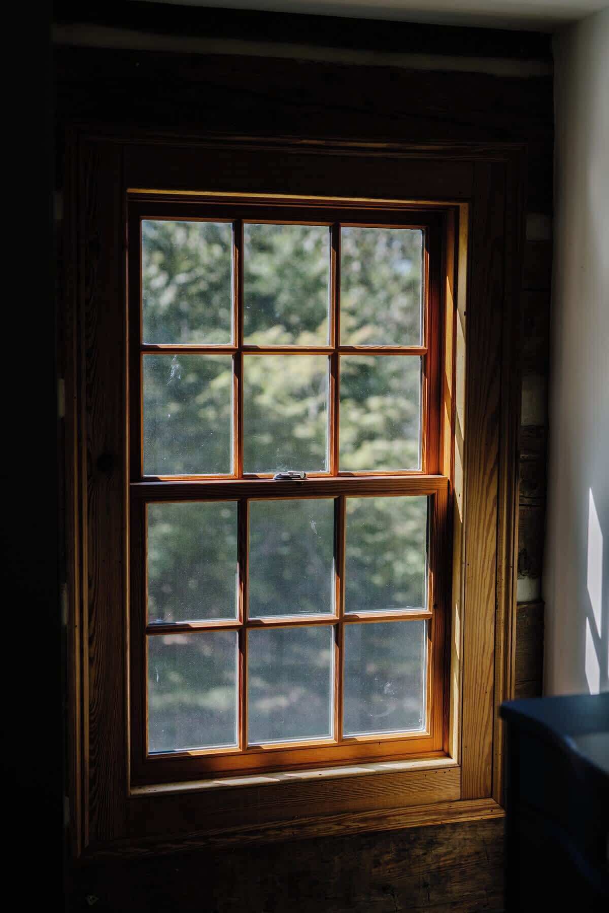 Una ventana con marco de madera y múltiples cristales, que deja entrar luz natural a una habitación con vistas a árboles.