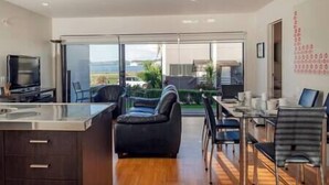A modern kitchen with a dining area, a black leather sofa, and a view of the outdoors.