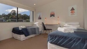 A hotel room with two beds, a desk, and a chair. There is a window providing a view of the outdoors.