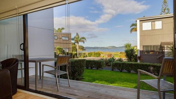 A balcony with a view of a landscaped garden and a distant coastline.
