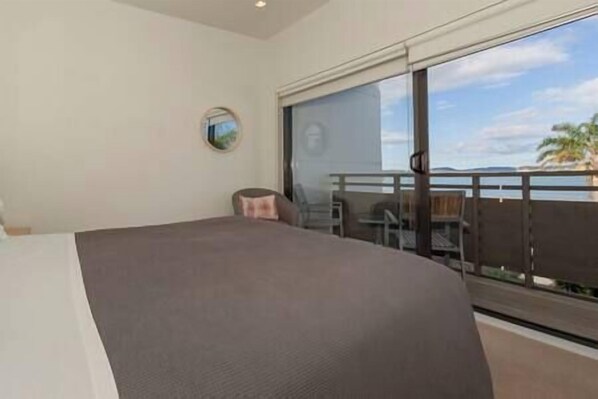 Ein Hotelzimmer mit einem großen Bett, einem runden Spiegel an der Wand und einem Balkon mit Meerblick.
