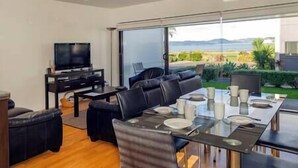 A modern living room with a large TV, a sofa, and a dining table set for four.