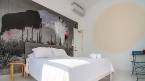 Een slaapkamer met een groot bed, een klein houten krukje, een deur en een muur met een groot rond ontwerp.