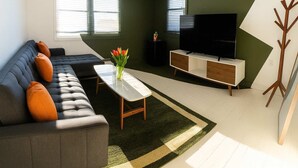 Een moderne woonkamer met een grijze bank, een bijzettafeltje, een televisie en een houten kapstok.