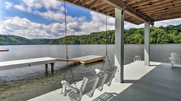 A wooden deck with a swing chair, a bench, and a chair by the water.