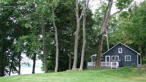 A house with a porch, surrounded by tall trees and a grassy area. - Brower Cottage - Lakefront Secluded Wooded Lot on Hutchins Lake Near Saugatuck (Fennville)