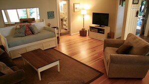 A living room with a sofa, a coffee table, and a TV stand. - Brower Cottage - Lakefront Secluded Wooded Lot on Hutchins Lake Near Saugatuck (Fennville)