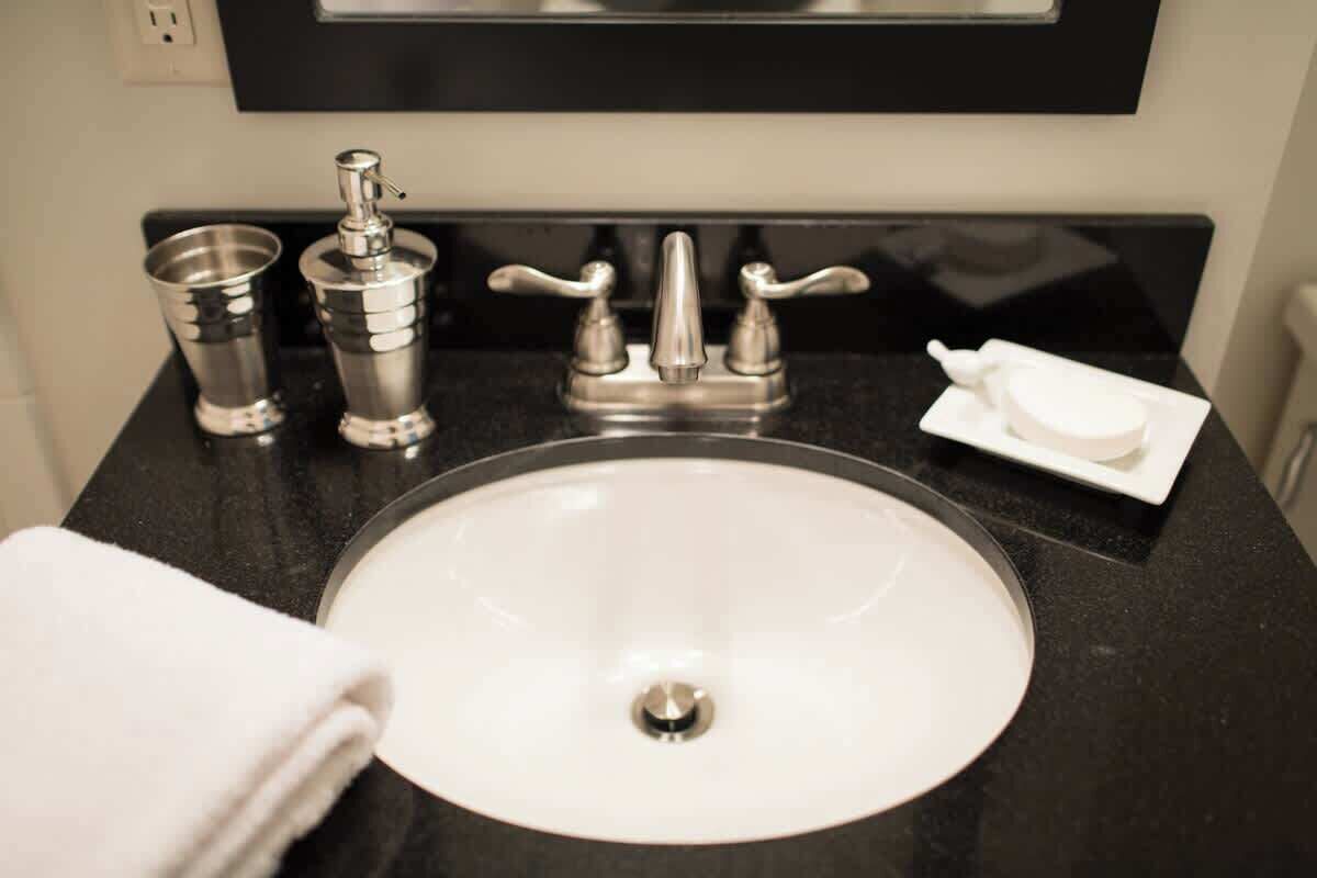 A bathroom sink with a faucet, a soap dispenser, a cup, and a towel.