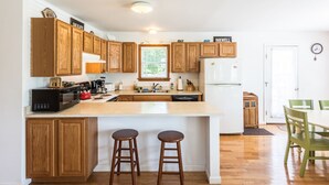 A kitchen with wooden cabinets, a white refrigerator, a coffee maker, and two stools. - Beautiful 3 bedroom  2 bath Home / Close to Town & Beach (Oak Bluffs)
