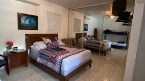 Une chambre à coucher comprenant un lit, une table de chevet, un ventilateur de plafond, une télévision et un miroir.