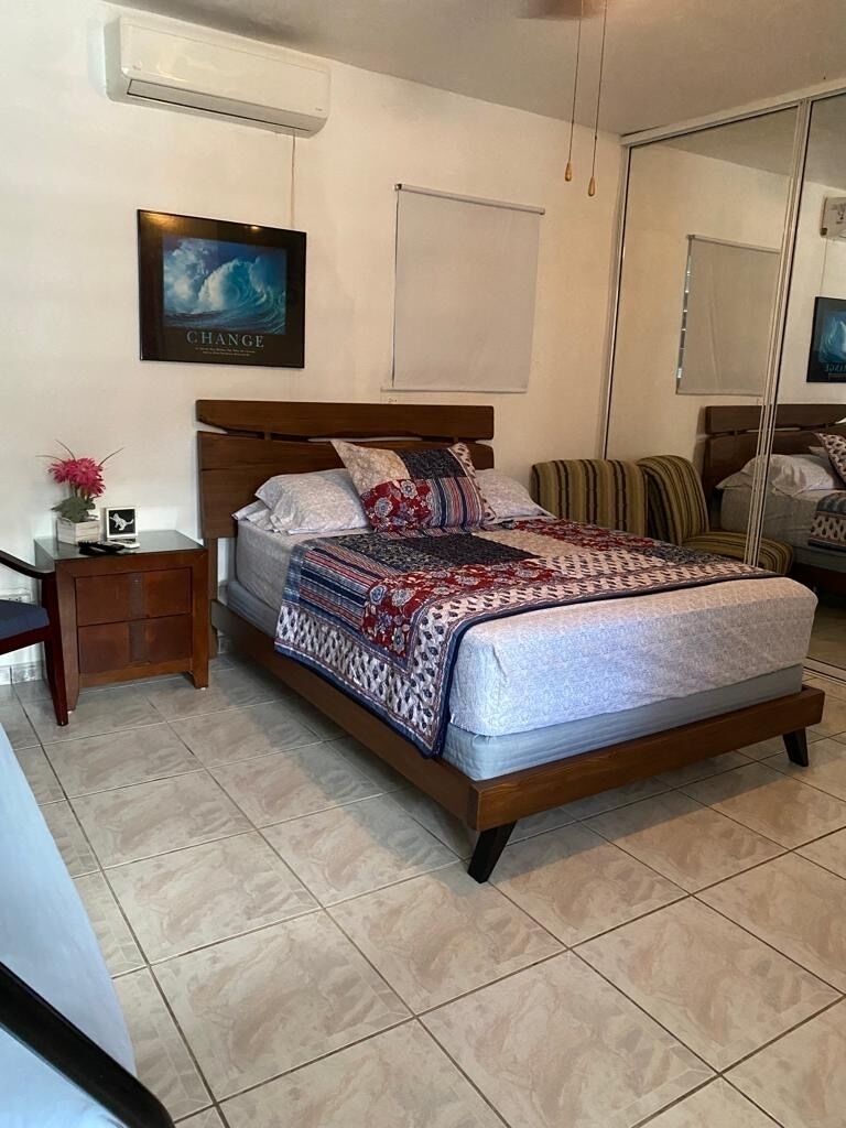 A bedroom with a bed, a nightstand, a mirror, and a wall-mounted air conditioner.
