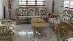 Un salon spacieux comprenant un ensemble de canapés, des fauteuils en osier, une table basse en verre et un luminaire suspendu au plafond.