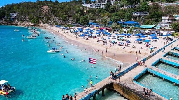 Une plage avec une jetée, une eau turquoise et limpide, et des parasols de plage.