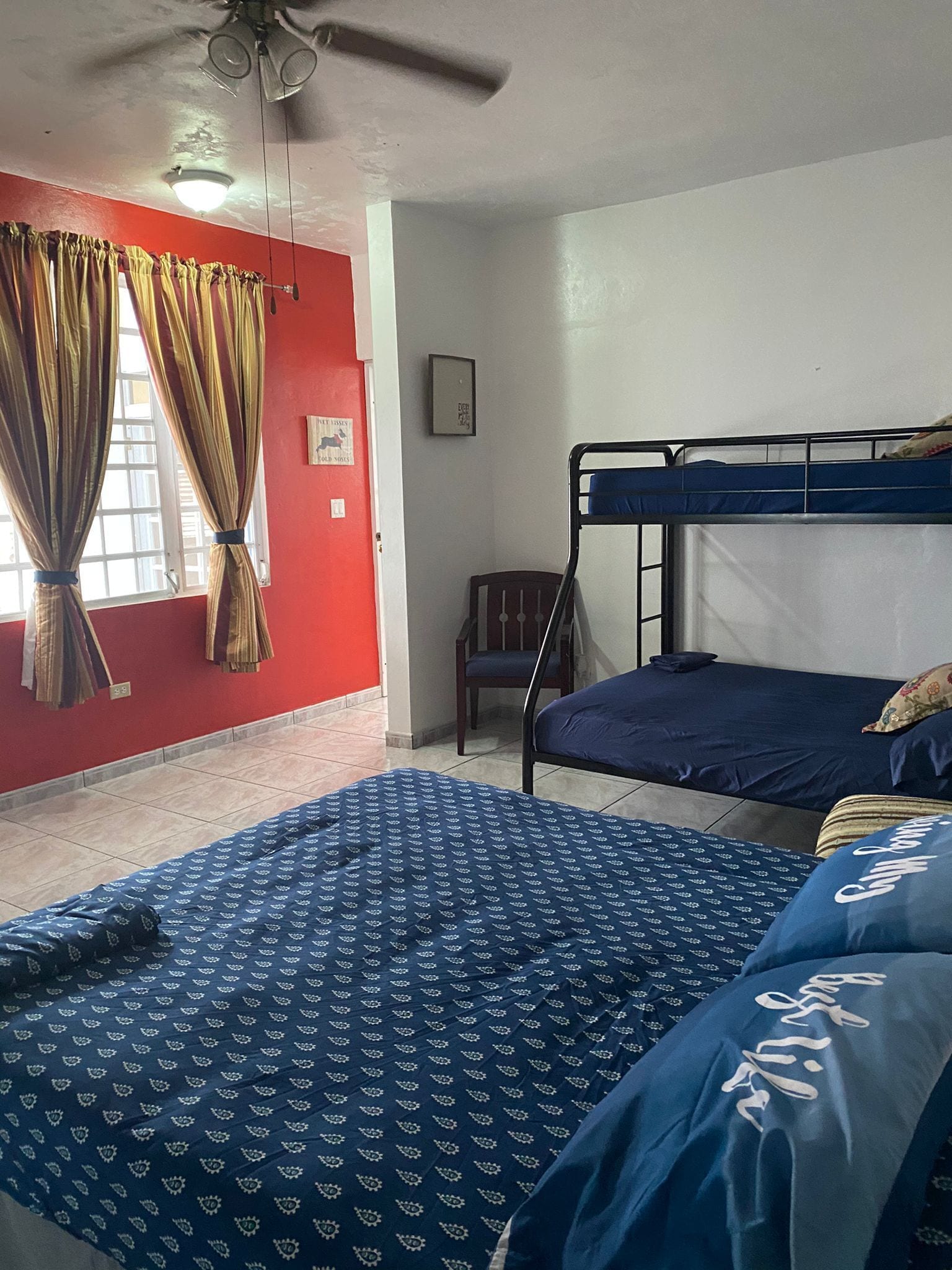 A room with a bed, a chair, a ceiling fan, and a window with curtains.