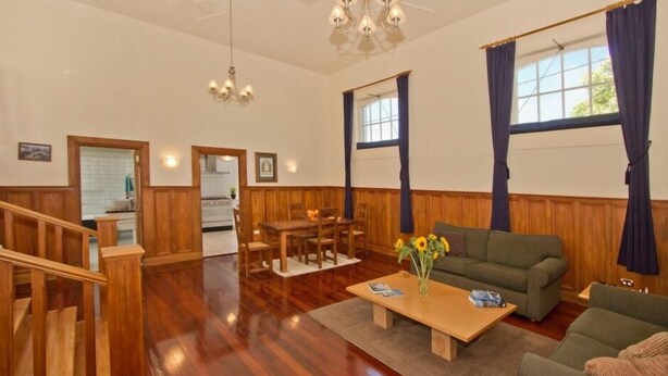 Un salón comedor amplio con suelo de madera, un sofá, una mesa de centro con un jarrón de flores y una zona de comedor con mesa y sillas.