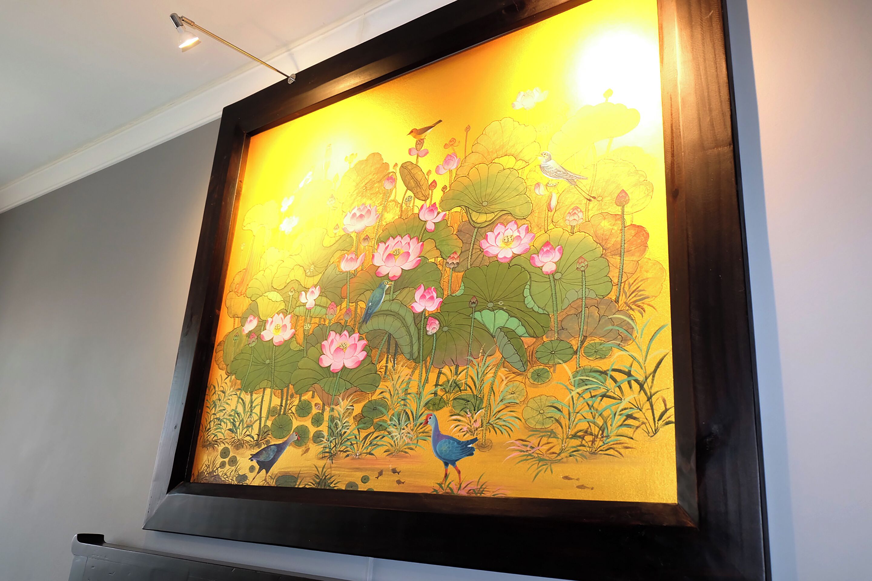A framed artwork of a pond with lotus flowers and birds.