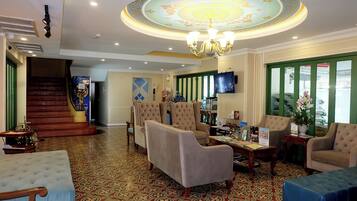 A lobby with a grand chandelier, a staircase, and a seating area with armchairs and a sofa.