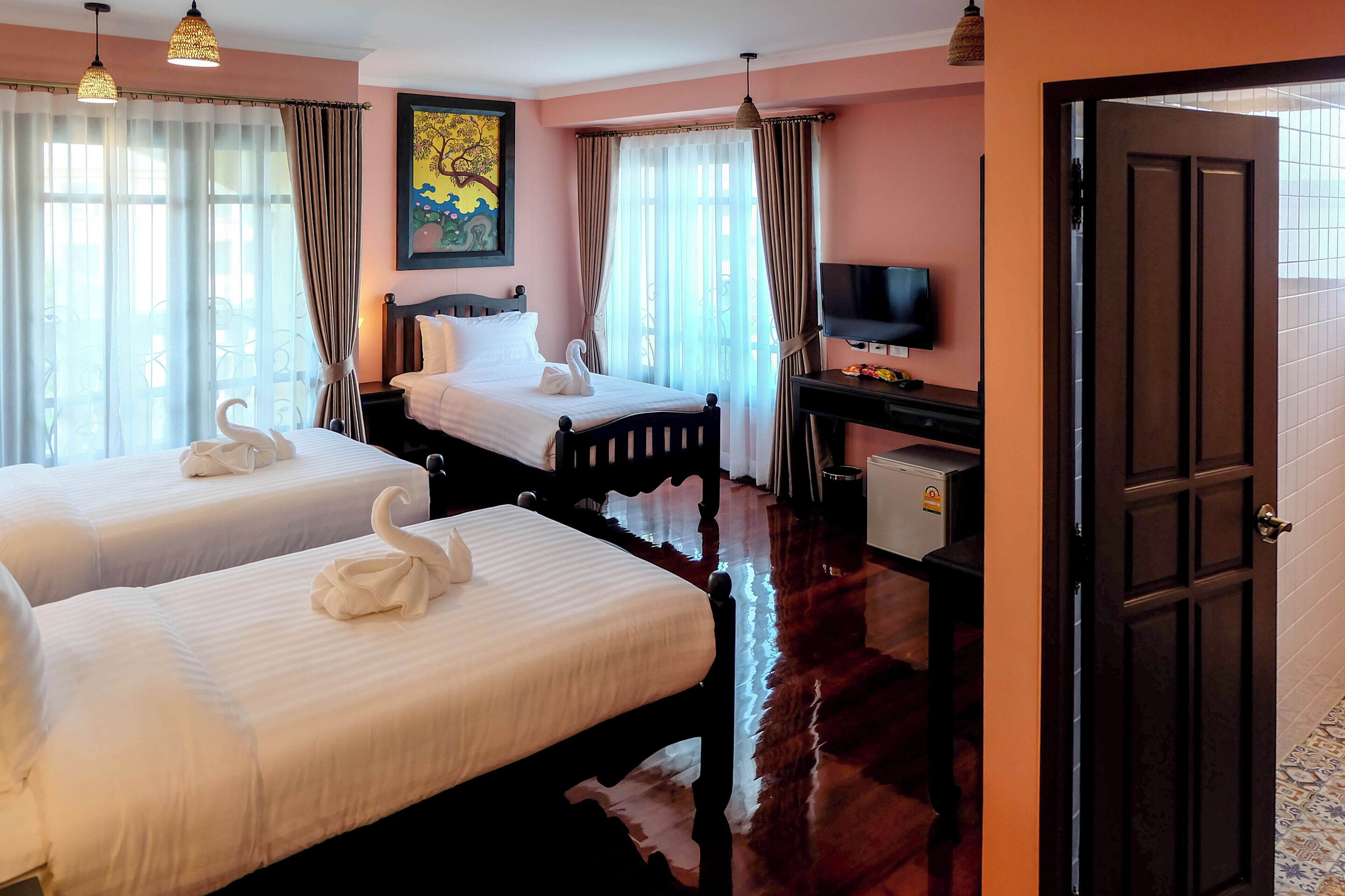 A hotel room with two beds, a desk with a television, and a door to the right.