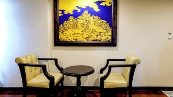 Una habitación con dos sillas y una pequeña mesa, una obra de arte enmarcada sobre la mesa, y una pared lisa.