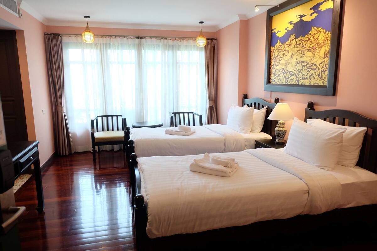 A hotel room with two beds, a desk, a chair, and a large decorative painting on the wall.