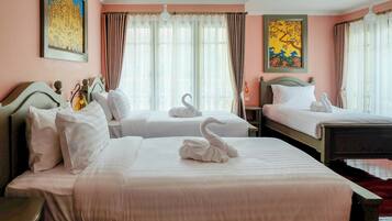 Quarto de hotel com duas camas, cada uma com roupa de cama branca e almofadas de cisne decorativas. Há janelas amplas com cortinas leves, um quadro na parede e uma luminária no teto.