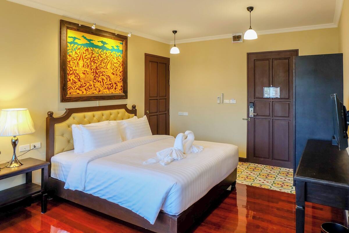 A hotel room with a bed, a nightstand, a lamp, a wall painting, a door, and a television.