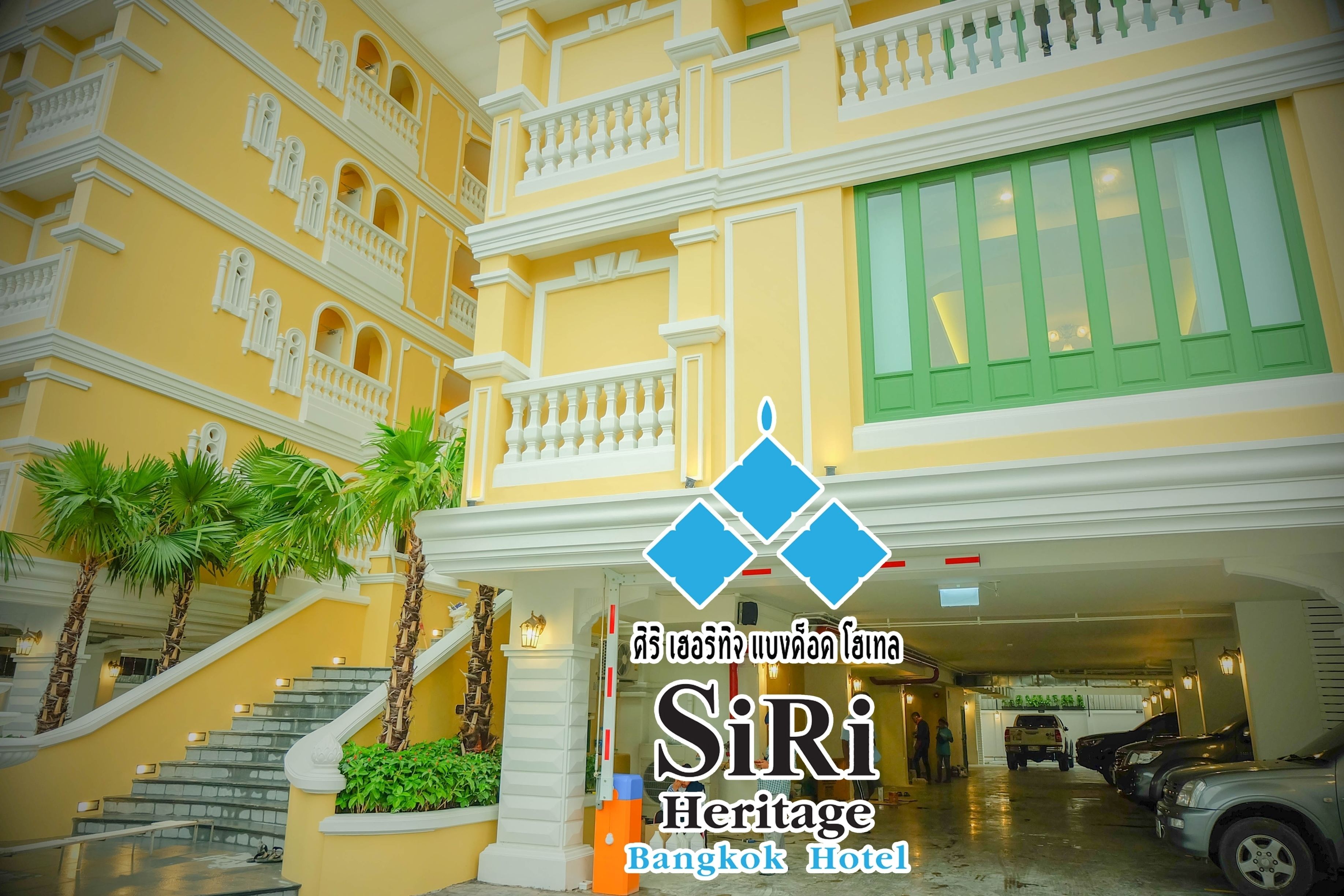 A multi-story hotel with a yellow facade, white balconies, and a green window.