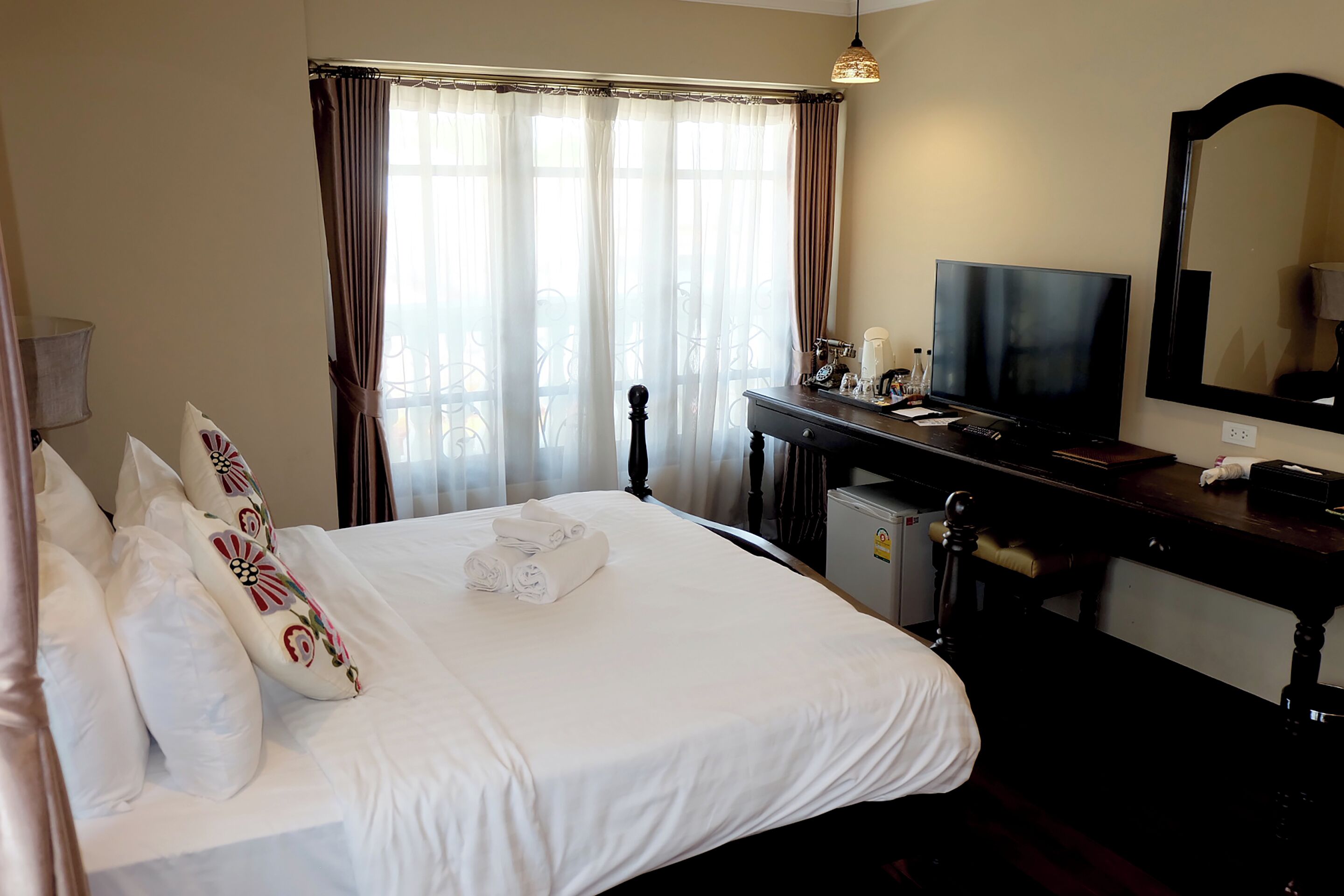 Una habitación de hotel con cama, televisión, escritorio con espejo y ventana con cortinas.