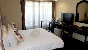 Una habitación de hotel con cama, televisión, escritorio con espejo y ventana con cortinas.