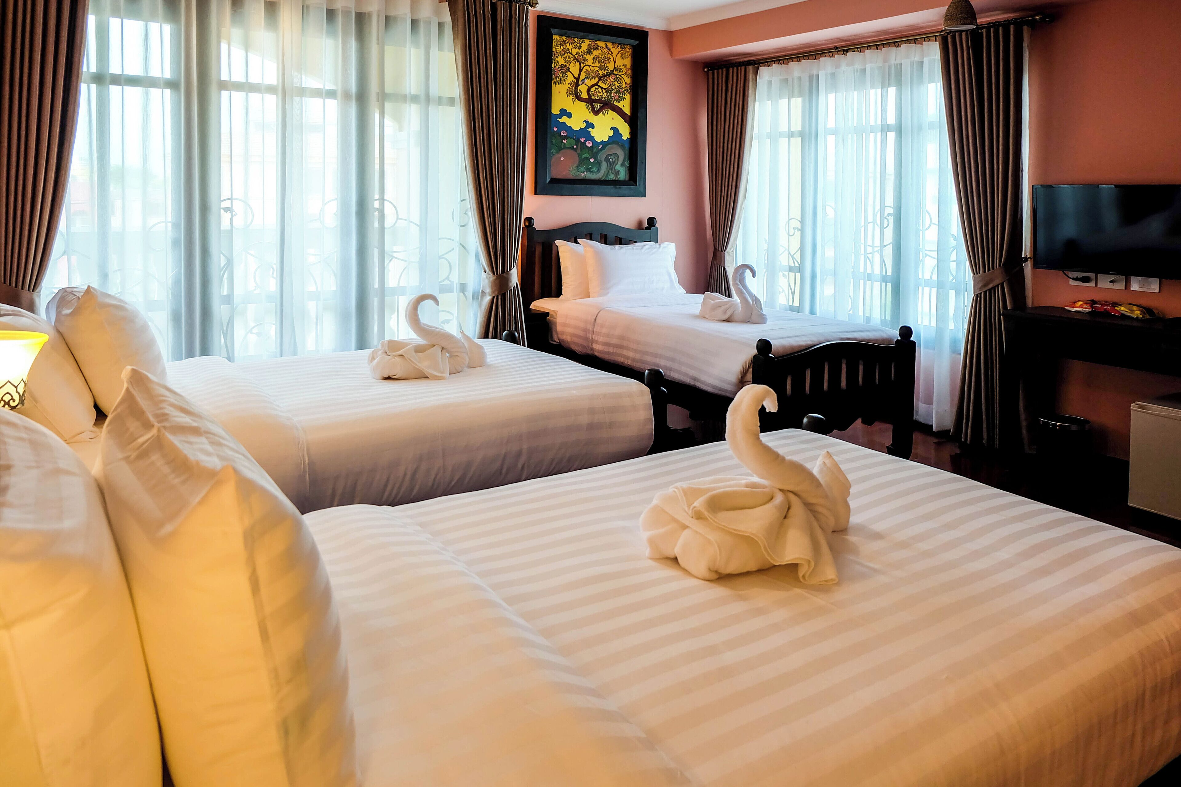 A hotel room with two beds, each with a swan-shaped towel, a painting on the wall, and a television on the dresser.