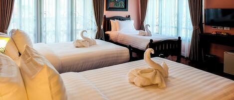 A hotel room with two beds, each with a swan-shaped towel, a painting on the wall, and a television on the dresser.