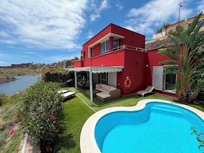 Ein rotes, zweistöckiges Haus mit Schwimmbad, überdachter Terrasse und Meerblick.